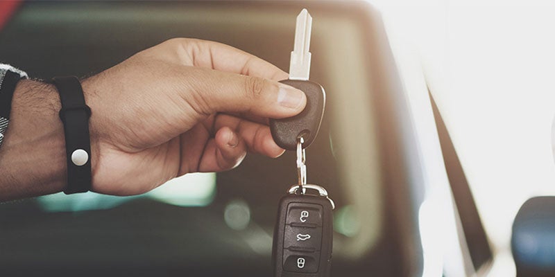 A person holds a car key in front of a parked car.