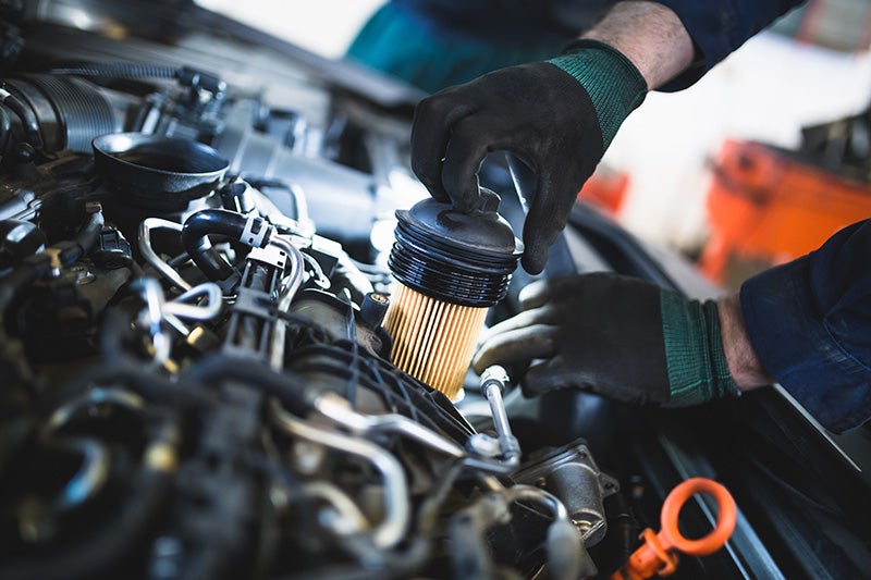 A man is focused on repairing a car engine, surrounded by tools and parts in a garage setting.