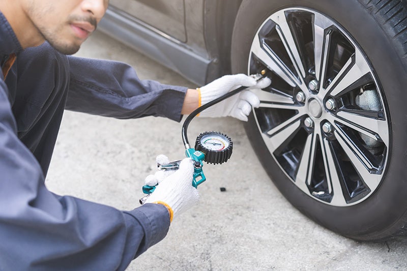 A man checks tire pressure using a gauge, ensuring proper inflation for safe driving.